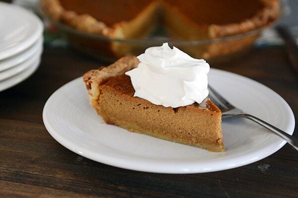 A slice of pumpkin pie with a dollop of whipped cream on it.