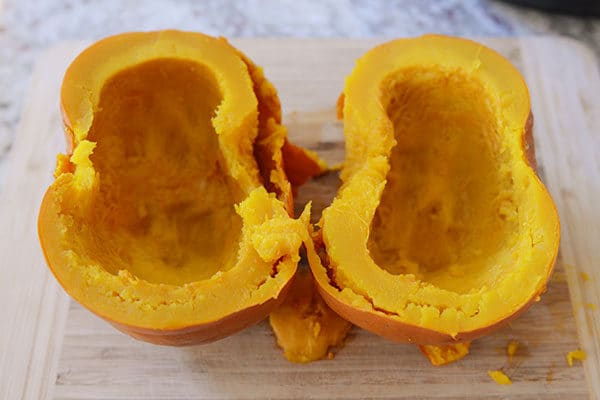 A cooked pumpkin cut in half on a wooden cutting board.