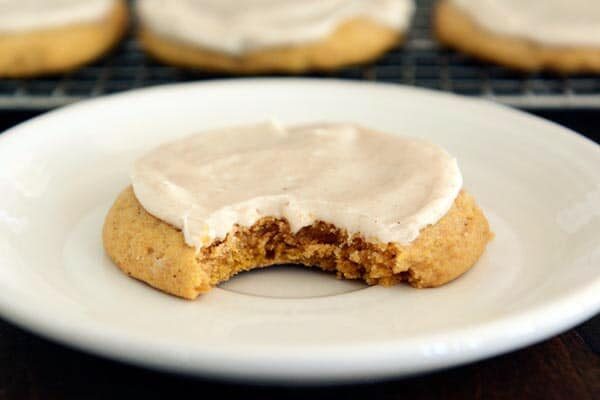 A frosted pumpkin sugar cookie with a bite taken out on a white plate.