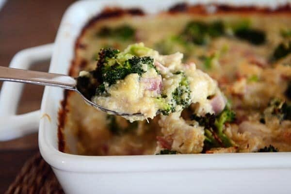 A white casserole dish full of a cheesy chicken, ham, and broccoli casserole.