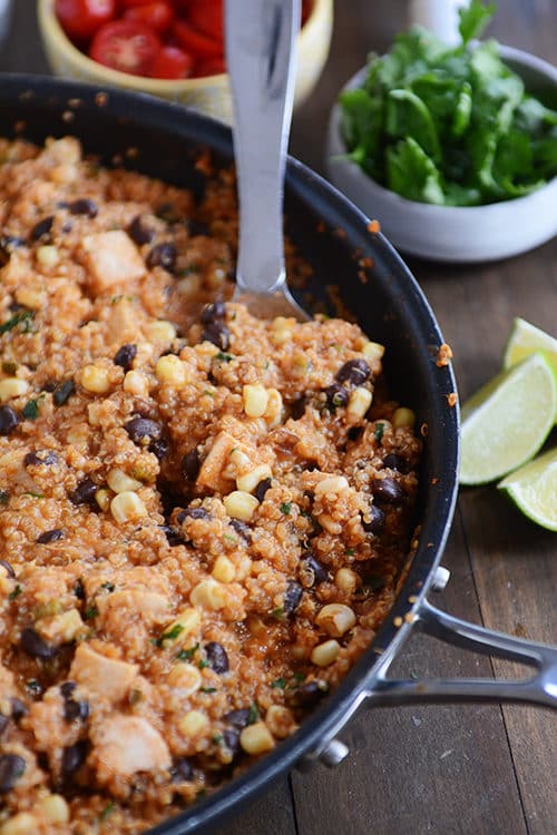 A large metal spoon taking a helping of a quinoa enchilada black bean meal out of a skillet.