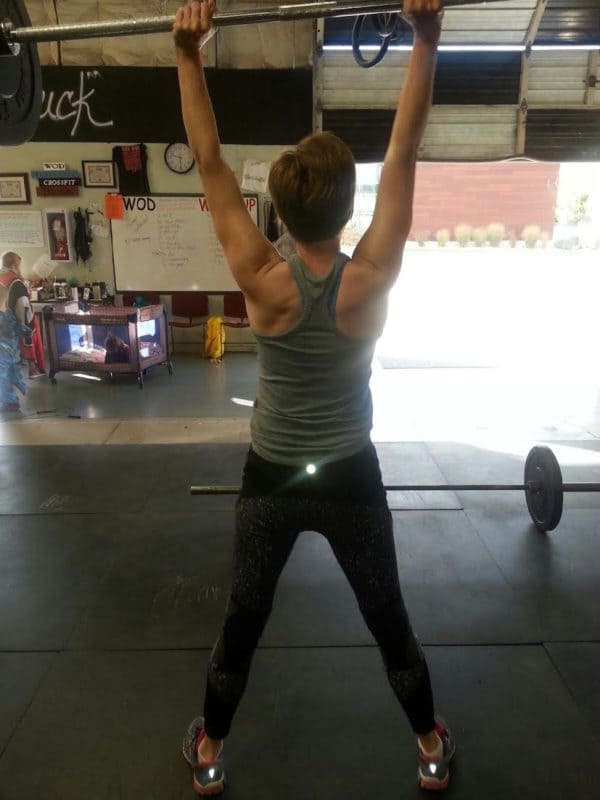 A lady lifting a barbell of weights over her head.