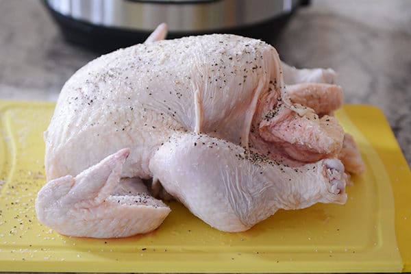 A raw whole chicken, sprinkled with pepper, on a yellow cutting board. 