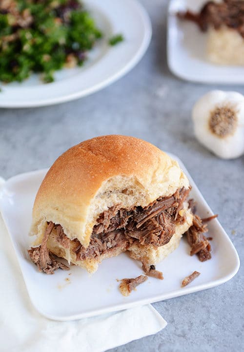 A square white plate with a half-eaten roll filled with shredded beef. 