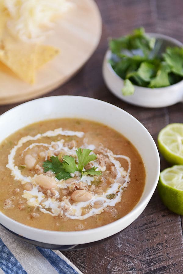 A white bowl of white bean chili with a swirl of cream and parsley on top.