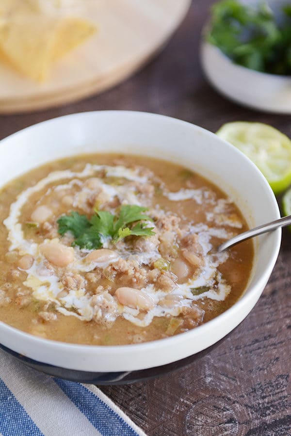 White bowl of white bean chili topped with parsley sprigs.