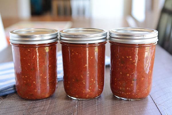 3 jars of homemade salsa lined up in a row on a wooden table. 