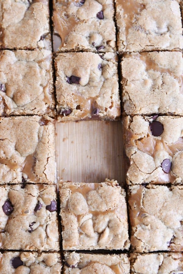 Slab of salted caramel brown butter chocolate chip bars cut into squares on wood cutting board.