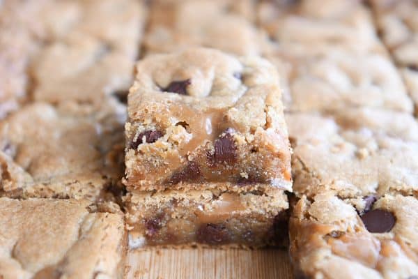 Slab of salted caramel brown butter chocolate chip bars cut into squares and two stacked on each other on wood cutting board.