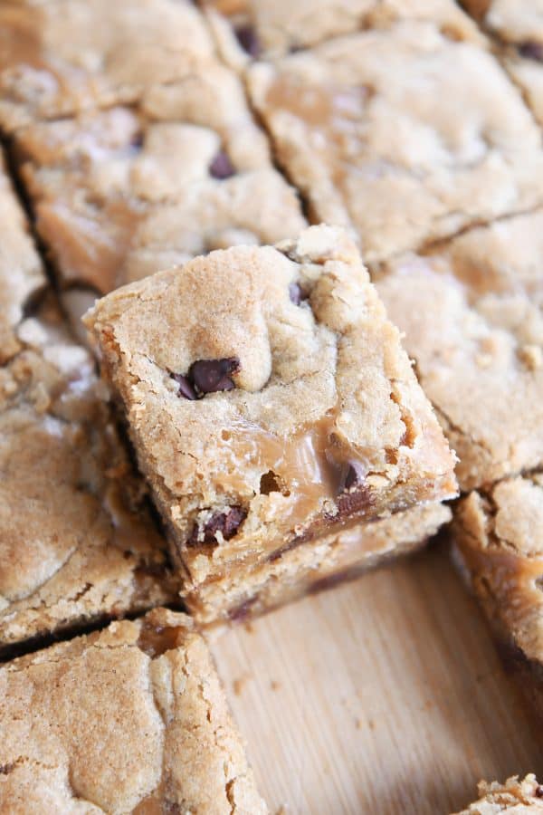 Slab of salted caramel brown butter chocolate chip bars cut into squares and two stacked on each other on wood cutting board.