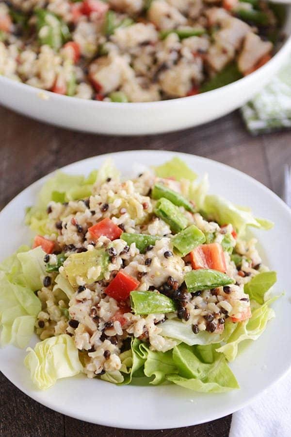 A white plate of green salad topped with a rice, tomato, and avocado mixture.