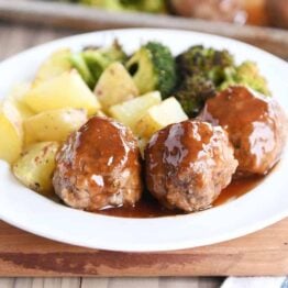 White plate filled with meatballs drizzled in sweet and sour sauce and roasted vegetables.