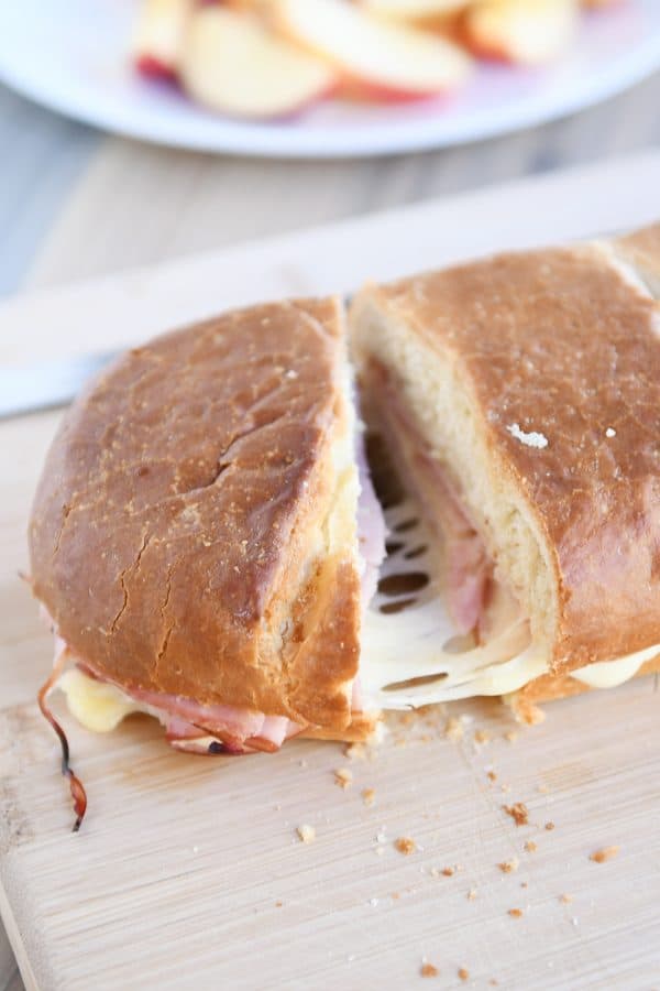 Cutting a slice of ham and cheese sheet pan panini on wood cutting board.