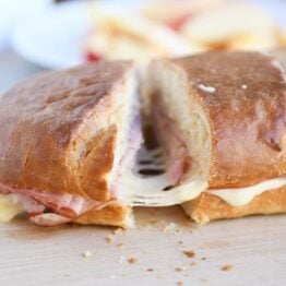 Cutting a slice of ham and cheese sheet pan panini on wood cutting board.