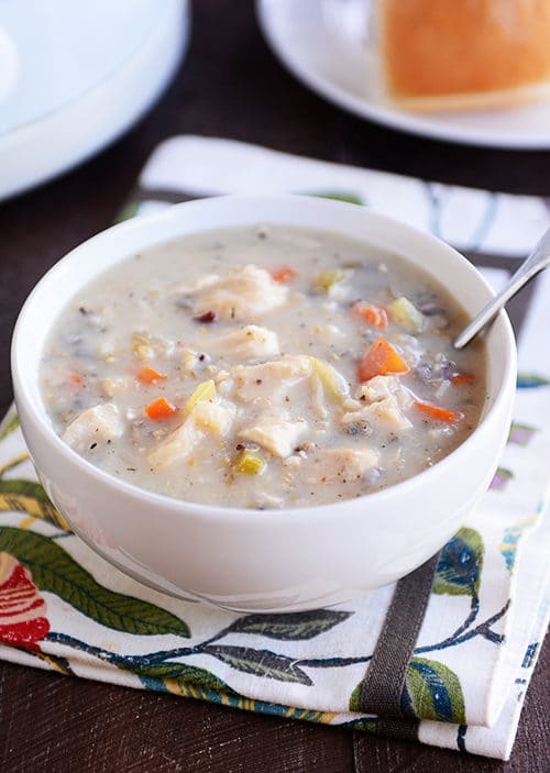 A white bowl full of creamy chicken, vegetable, and rice soup.