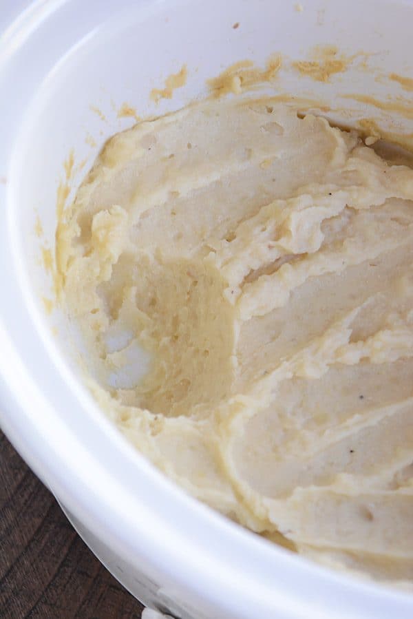 A white crockpot full of mashed potatoes.