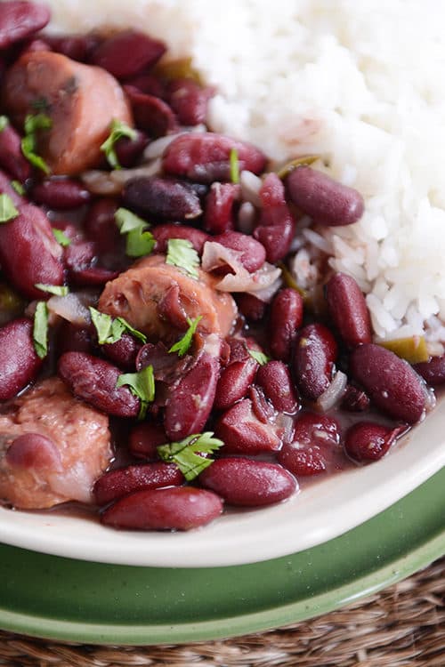 A white plate of cooked chicken sausage and red beans next to cooked white rice.
