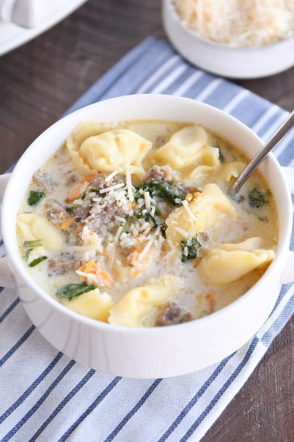Spoon in white bowl with slow cooker tortellini sausage spinach soup.
