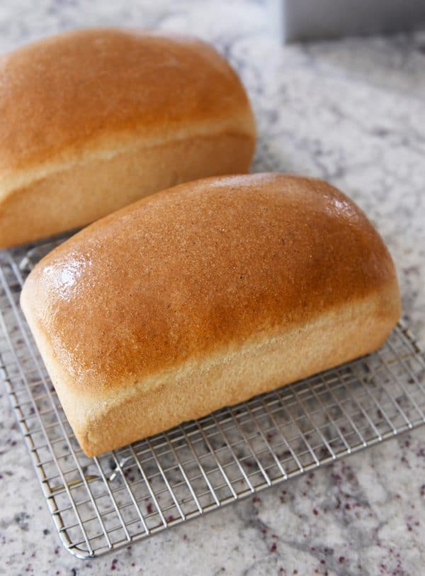 Two loaves of small batch whole wheat bread slathered in butter on cooling rack. 