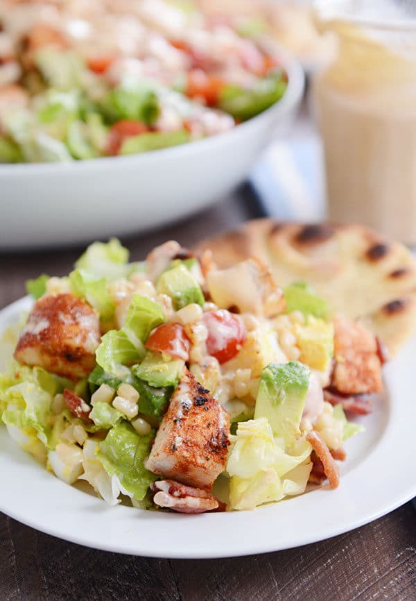 A grilled chicken cobb salad next to a flatbread on a white plate.