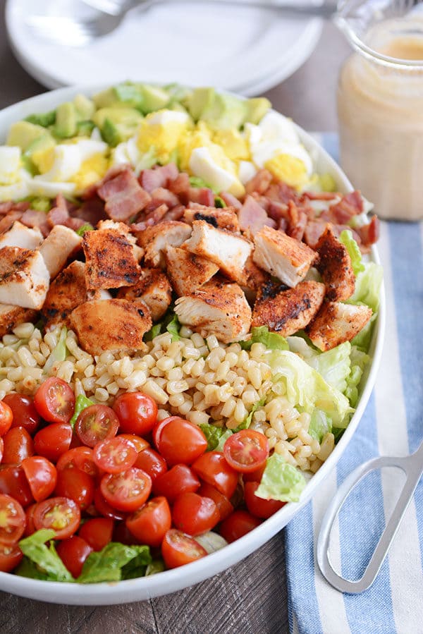 A large oval white bowl filled with tomatoes, rice, grilled chicken pieces, diced boiled egg, and diced avocado.
