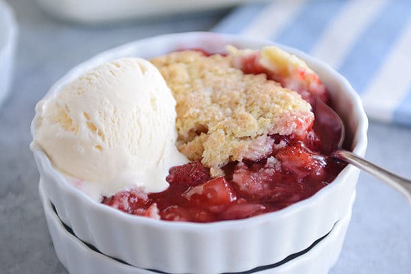 A small white ramkein with strawberry cobbler and a scoop of vanilla ice cream.