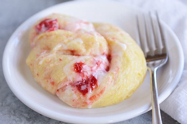 A strawberry cream cheese roll on a white plate, with a fork laying next to it. 