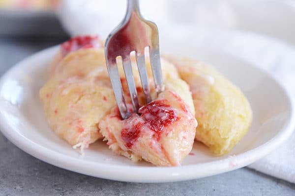 A strawberry cream cheese roll on a plate with one bite cut out on a fork ready to eat. 