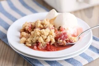 White plate with scoop of strawberry rhubarb crumble and vanilla ice cream.