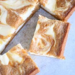 Swirled carrot cake cheesecake bars cut into squares; top down view.