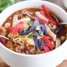 White bowl filled with taco soup, cheese, sour cream and tortilla strips.