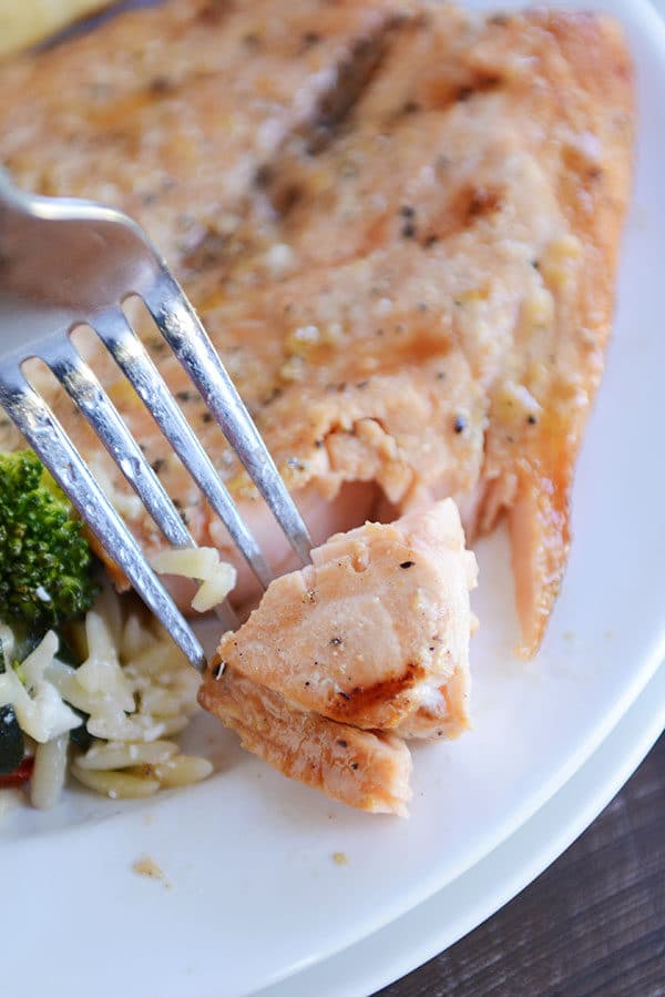 A fork taking a bite out of a grilled fillet of salmon.