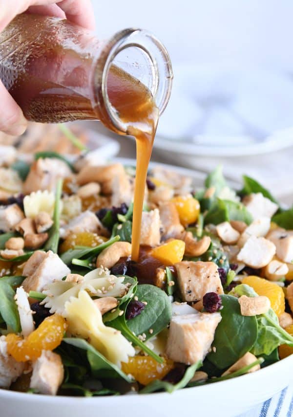 Pouring teriyaki dressing over bowtie pasta salad. 