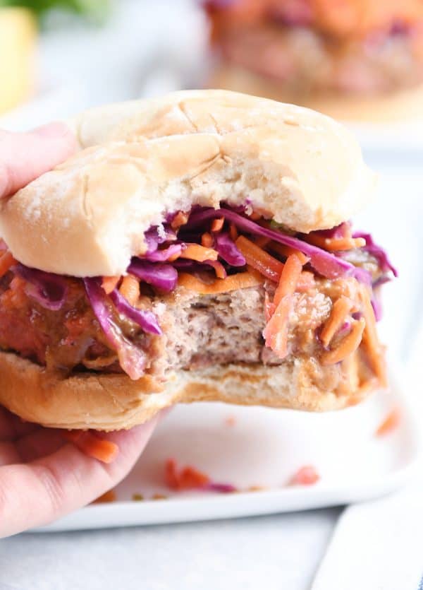 Bite taken out of Thai burgers on white plate.