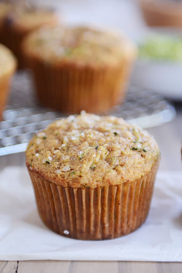 A zucchini muffin on a piece of parchment with other muffins in the background on a cooling rack.