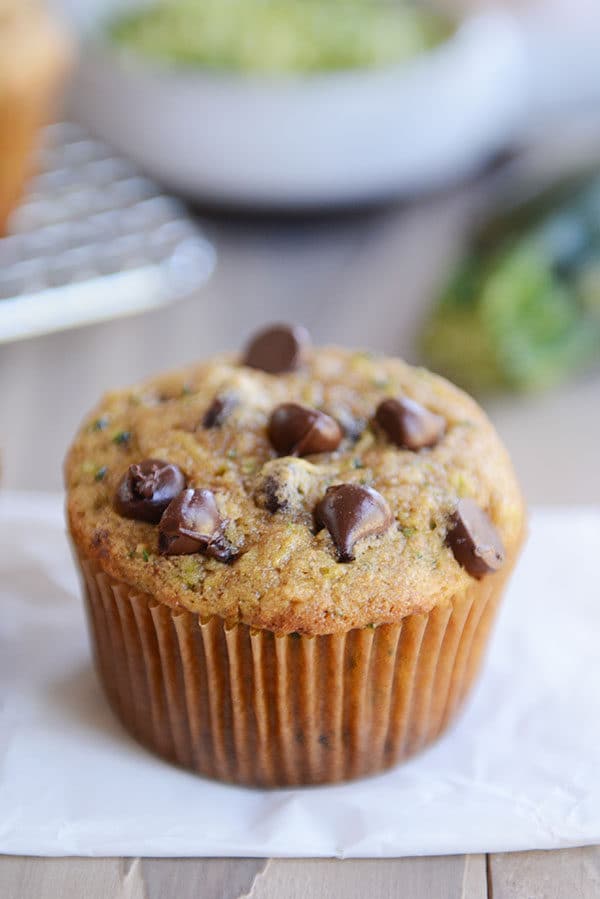 A chocolate chip topped zucchini muffin on a piece of parchment paper.