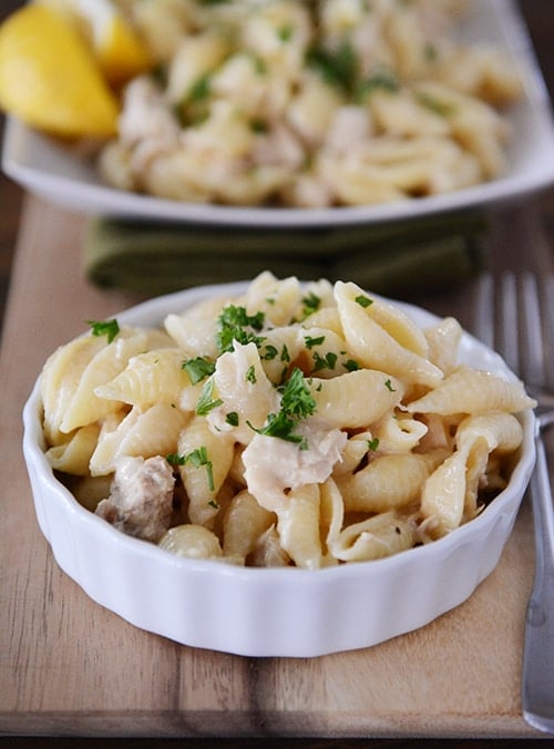 A small white ramekin with cooked pasta and tuna and a platter of more behind it.