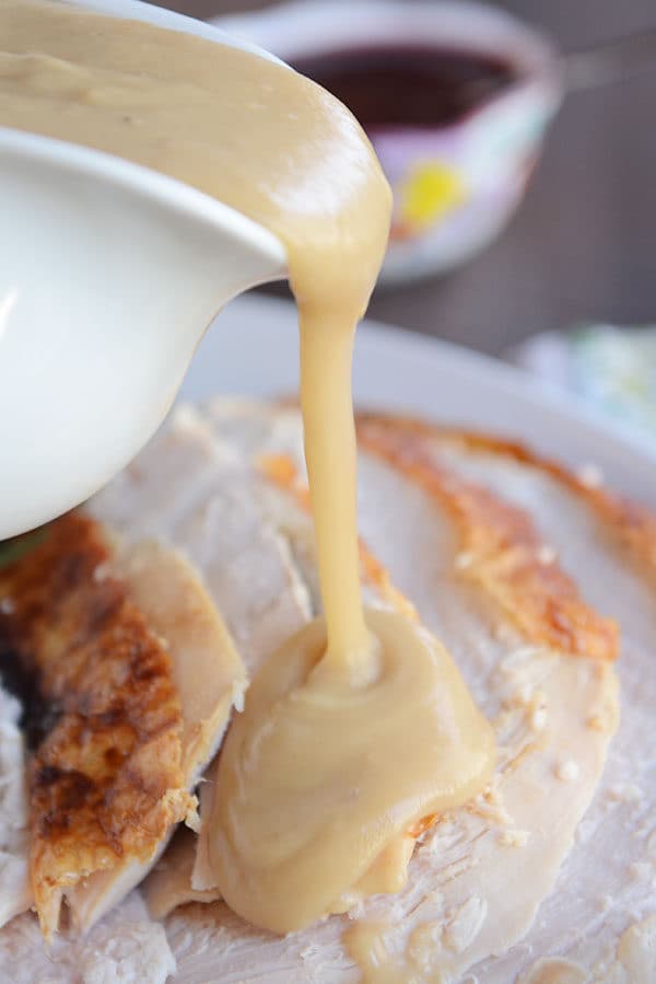 Brown gravy getting poured over thick slices of roast turkey.