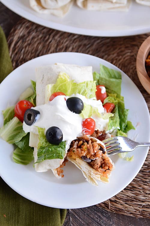 A turkey and rice burrito covered in toppings getting a bite taken out with a fork.