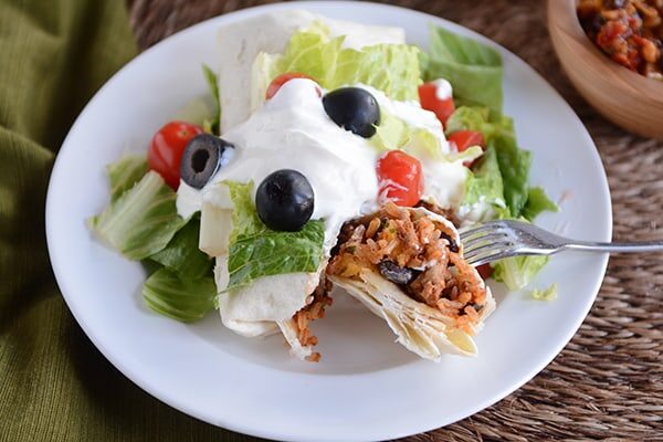 A ground turkey and rice burrito with toppings on a white plate.