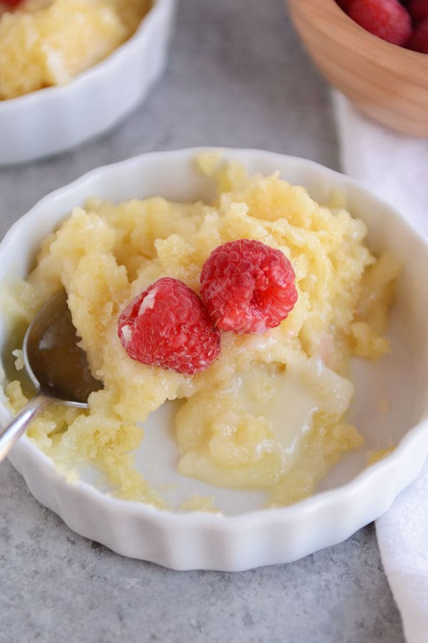 Top view of a ramekin of pudding cake and fresh raspberries with some bites taken out.