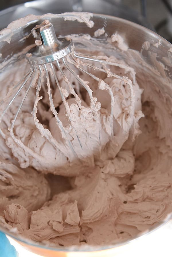 Chocolate whipped frosting in a metal KitchenAid bowl with the whisk on top.