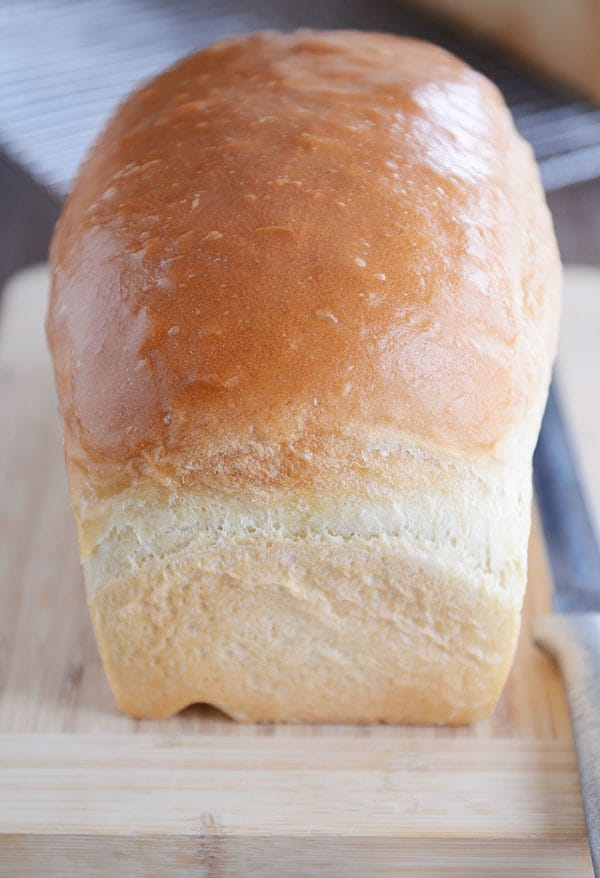 A loaf of homemade white bread on a wooden cutting board. 