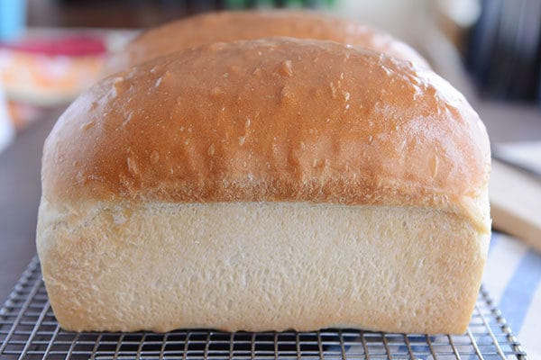 Two loaves of golden brown homemade white bread on a cooling rack.
