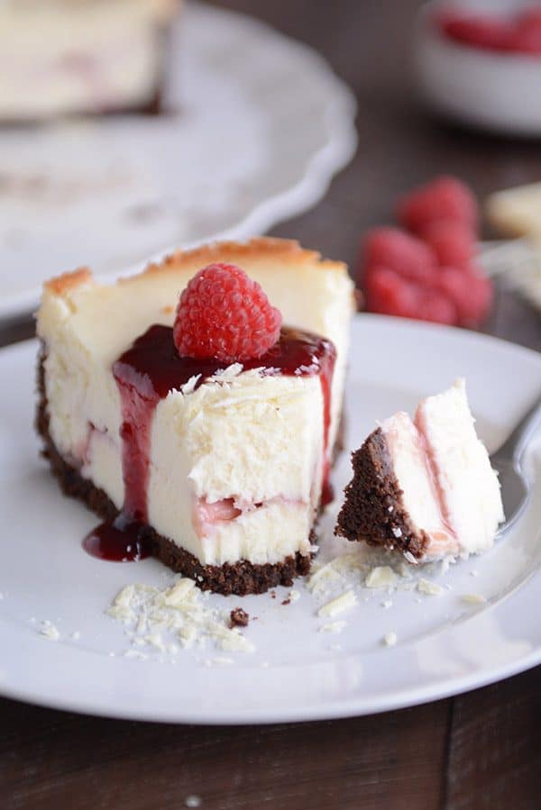 A fork taking a bite out of a white chocolate raspberry cheesecake. 