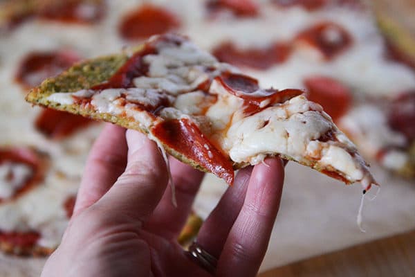 Hand holding a piece of pepperoni pizza with a bite taken out.
