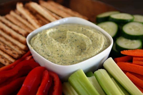 A tray of cut up vegetables and pretzel sticks with a bowl of zucchini hummus in the middle.